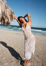 Woman in a paz dress crochet dress standing on a beach with ocean and clear sky in the background