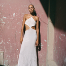 Woman in a white dress standing against a textured wall.