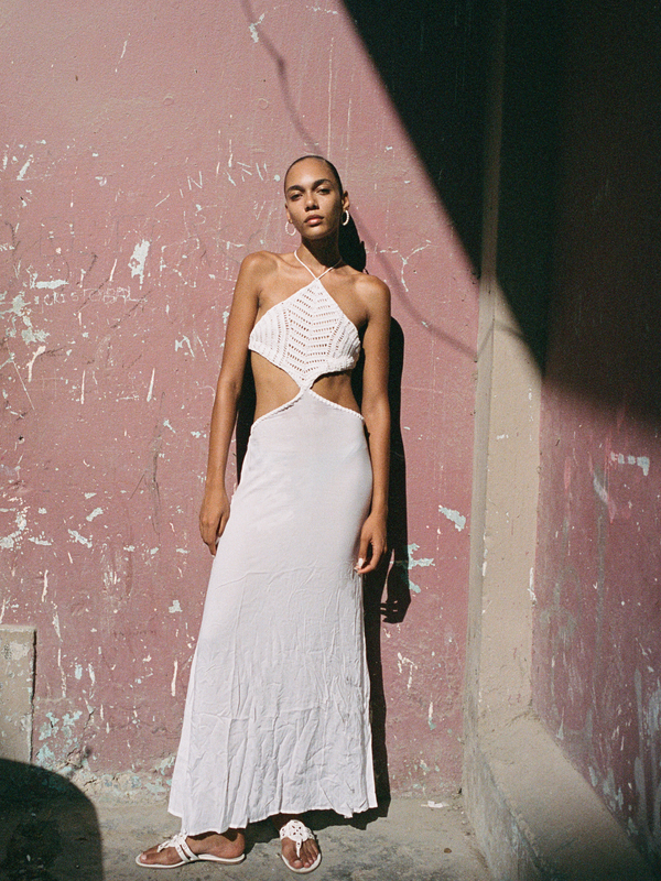 Woman in a white dress standing against a textured wall.